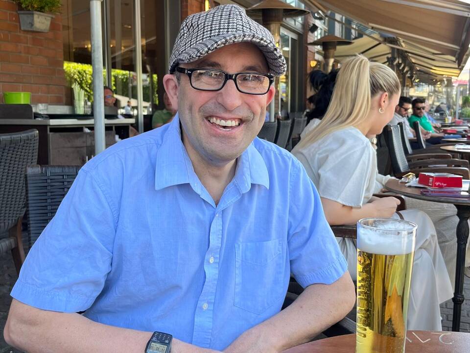 Ein Mann mit Brille, sitzt an einem Tisch und ein Bier steht darauf.