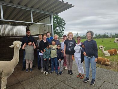 Gruppenfoto vor einem Stall und einer Wiese der Alpakas.