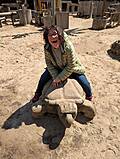EIne Person sitzt auf einer Holzschildkröte die am STrand steht.