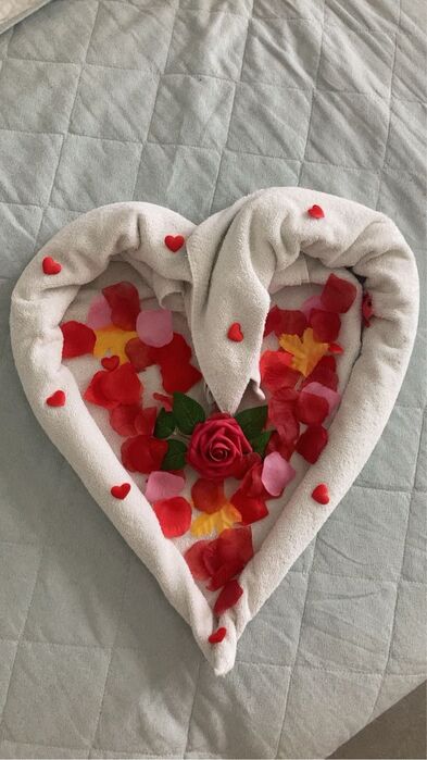 Bettdekoration mit weißen Handtüchern und Rosenblättern.