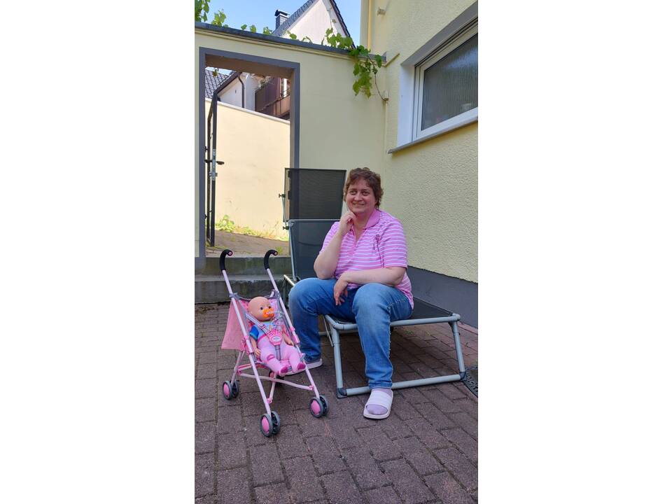 Eine Frau sitzt auf einer Sonnenliege, daneben steht ein Puppenbuggy.