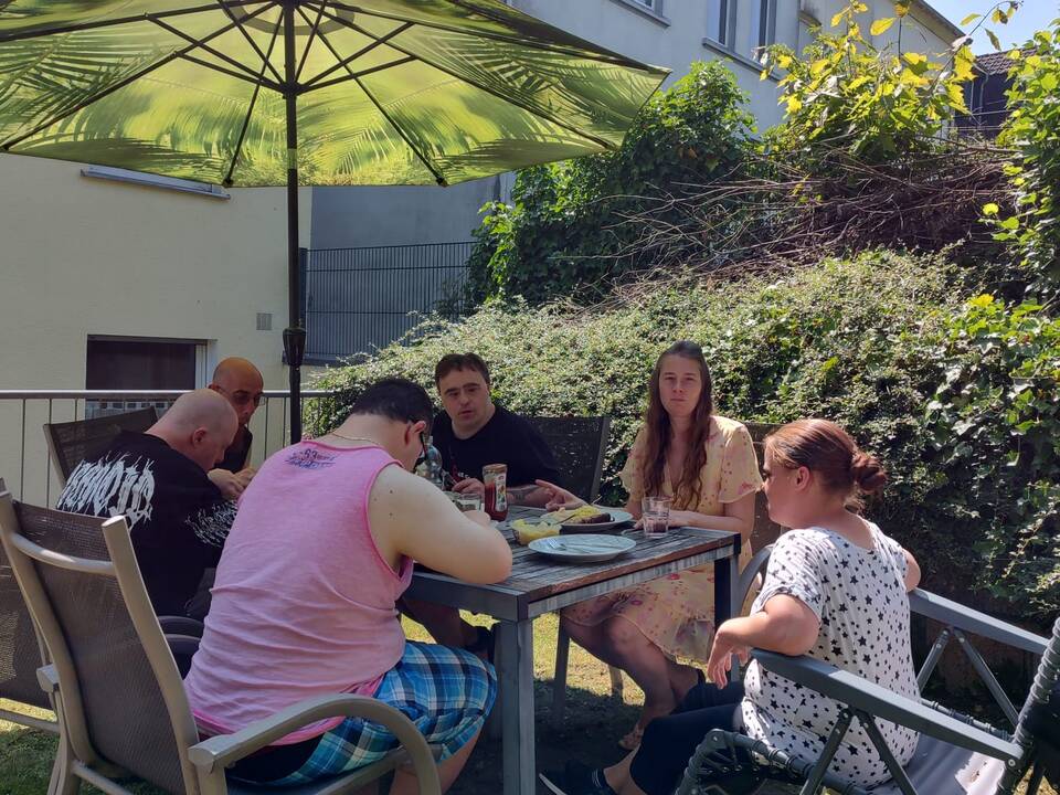 Mehrere Personen sitzen am Tisch im Garten und essen.