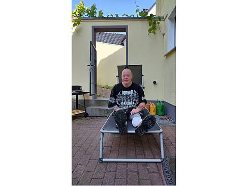 Ein Mann sitzt im Schatten auf einer Sonnenliege.
