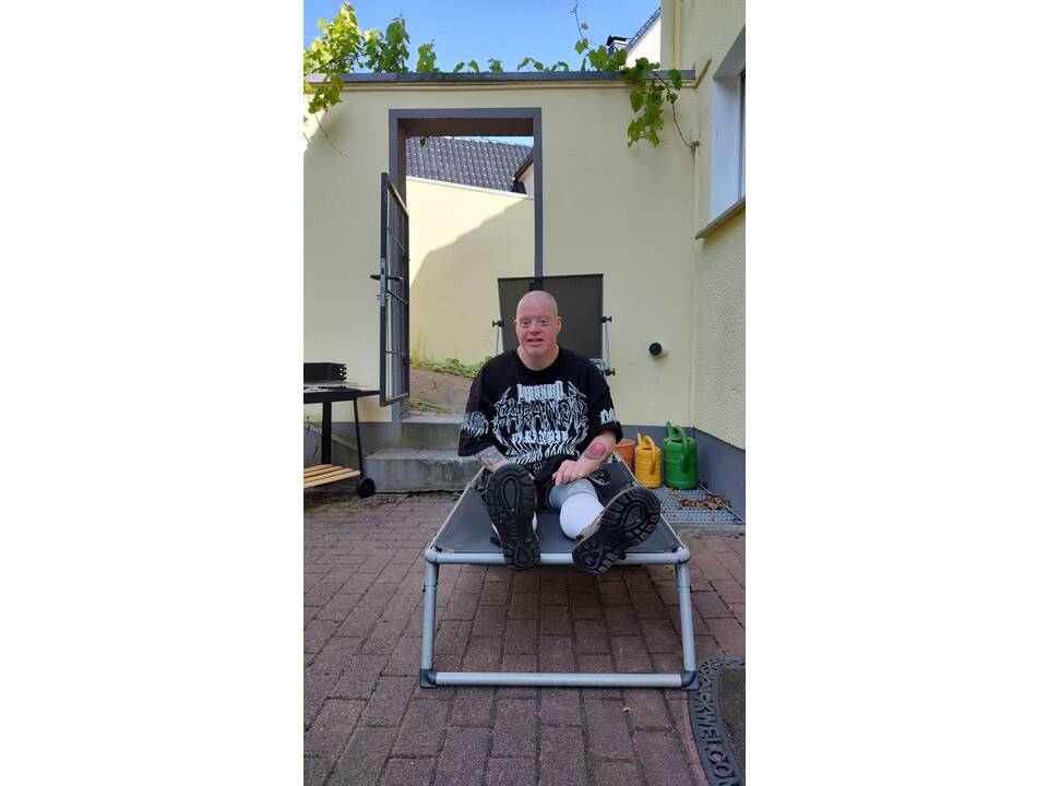 Ein Mann sitzt im Schatten auf einer Sonnenliege.