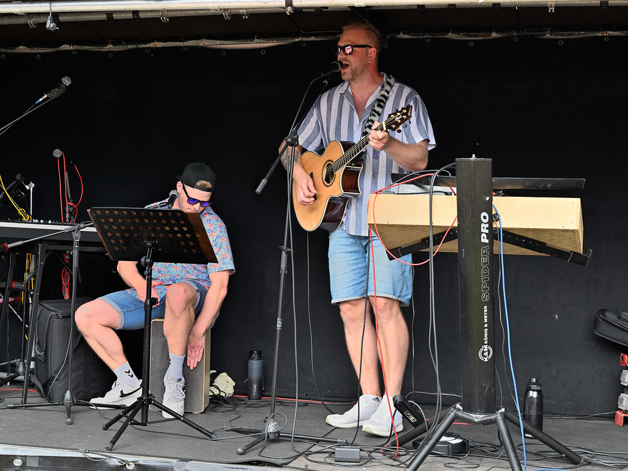 Zwei Personen auf der Bühne, einer mit einer Gitarre und der andere mit einem Cachon.