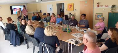 Viele Menschen sitzen an einem großen, langen Tiscsh in einem Raum.