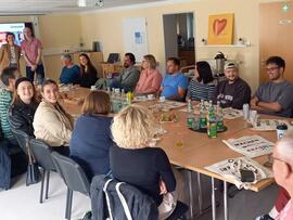 Viele Menschen sitzen an einem großen, langen Tiscsh in einem Raum.