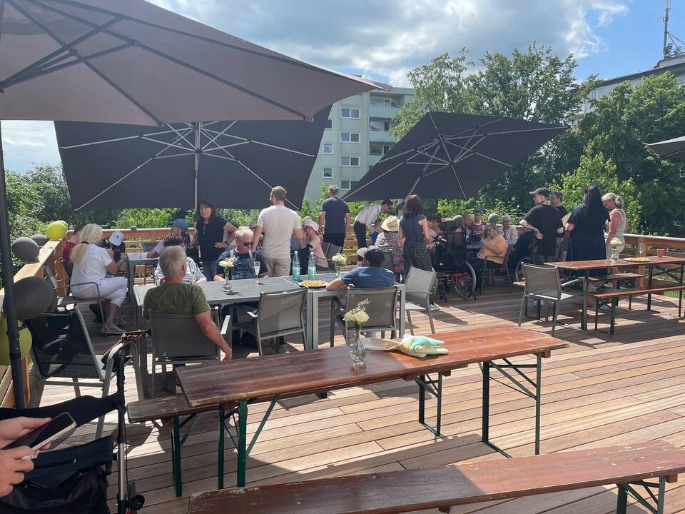 Menschen sitzen auf Bierzelt Garnituren unter Sonnensschirmen