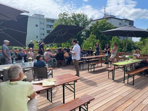 Menschen, Bierzeltgarnieturen und Sonnenschirme auf der Terasse.