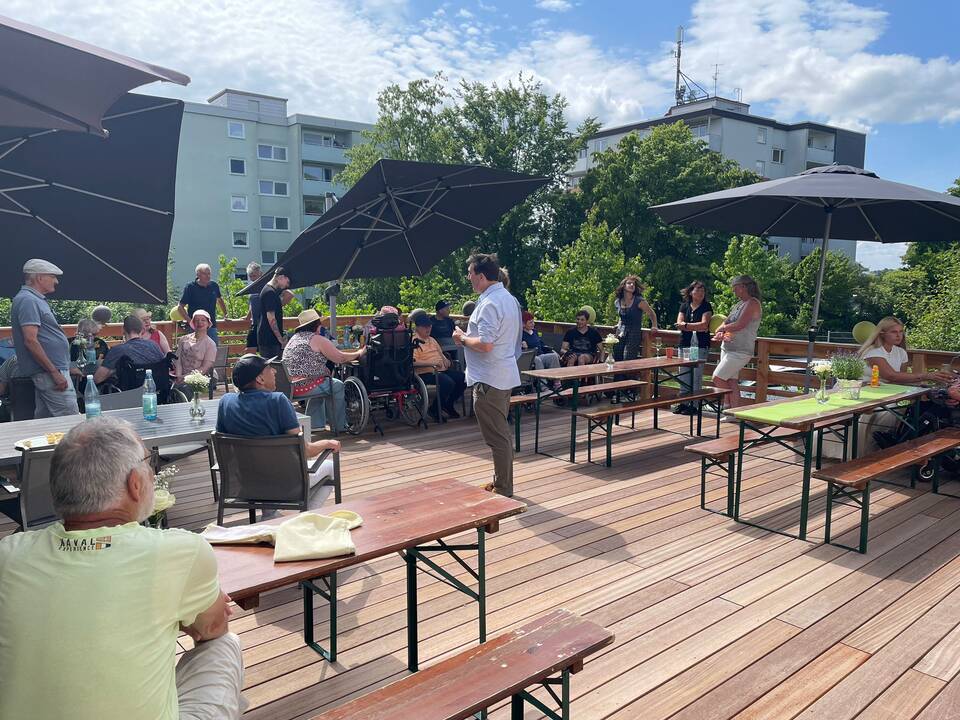 Menschen, Bierzeltgarnieturen und Sonnenschirme auf der Terasse.
