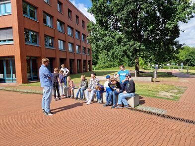 Mehrere Kinder und Jugendliche sitzen drausssen in der Sonne.