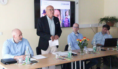 Jörg Bachmann, Sven Sieburg und Stephan Thiel sitzen an einem Tisch und Dr. Schröder steht daran.