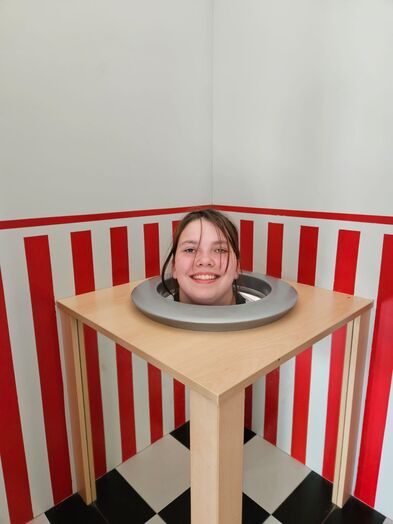 Eine Jugendliche in einem Kasten und nur der Kopf schaut raus. 
