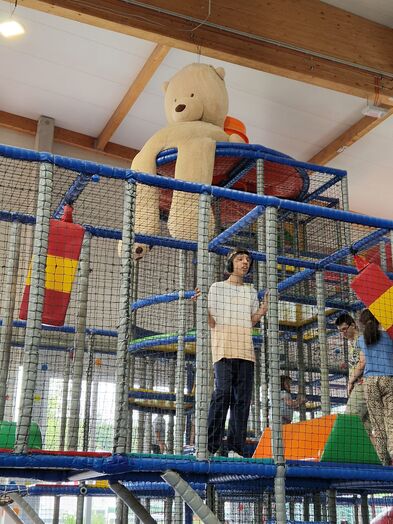 Ein Indoorkletterpark und oben drauf sitzt ein sehr großer Teddybär.