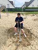 Ein Jugendlicher auf einem kleinen Bagger in einem großen Sandkasten.