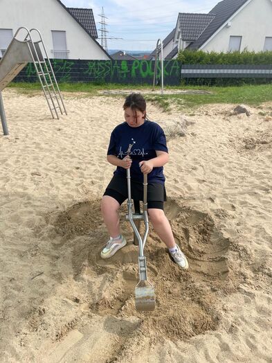 Ein Jugendlicher auf einem kleinen Bagger in einem großen Sandkasten.