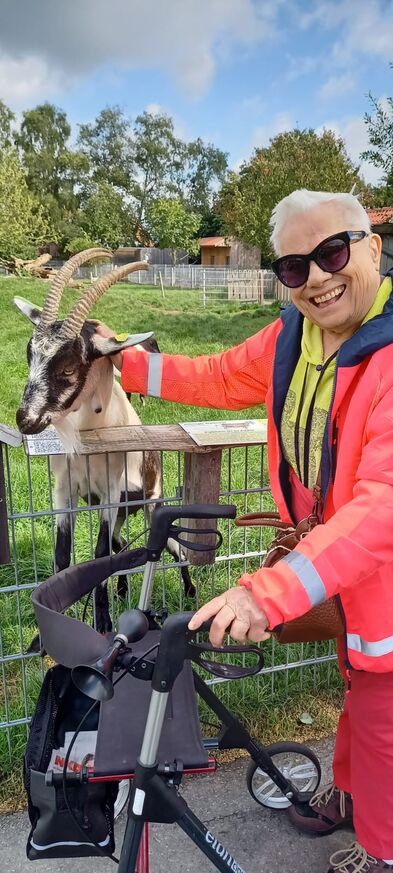 EIn Mann mit Rollator streichelt eine Ziege.
