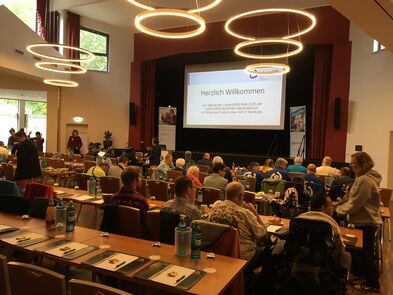 Viele Menschen sitzen an Tischen in einem großen Saal.