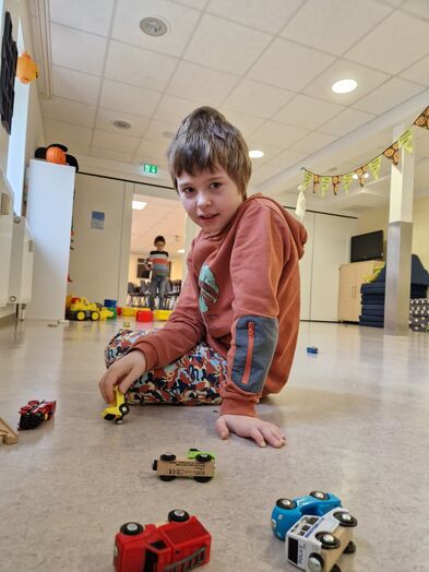 Ein Junge sitzt auf dem Boden und spielt mit Holzautos.