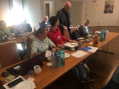 Mehrere Personen sitzen an Tischen, auf einem Tisch steht ein Laptop.