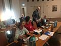 Mehrere Personen sitzen an Tischen, auf einem Tisch steht ein Laptop.
