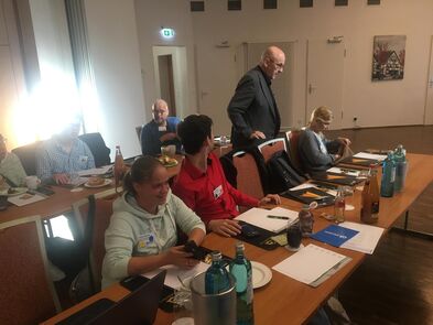 Mehrere Personen sitzen an Tischen, auf einem Tisch steht ein Laptop.