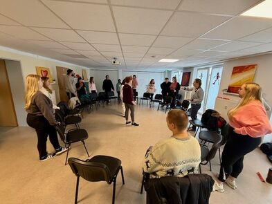 Viele Menschen in einem Raum um einen Stuhlkreis herum.