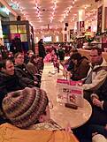 Viele Personen in einem Cafe an einem langen Tisch.