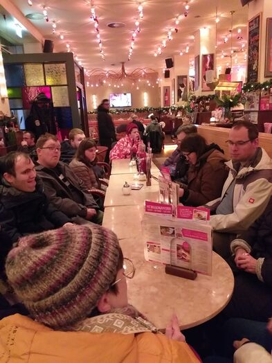 Viele Personen in einem Cafe an einem langen Tisch.