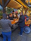 Menschen mit und ohne Hilfsmittel stehen mit Essen an einem großen Stehtisch der überdacht ist.