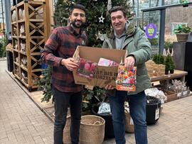 Zwei Männer stehen vor einem Weihnachtsbaum und halten eine Karton mit Blumenzwiebeln in der Hand.
