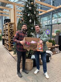 Zwei Männer stehen vor einem Weihnachtsbaum und halten eine Karton mit Blumenzwiebeln in der Hand.