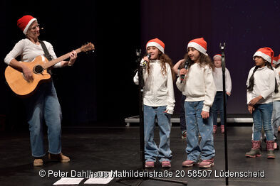 Eine Frau mit Gitarre und zwei Mädchen singen.