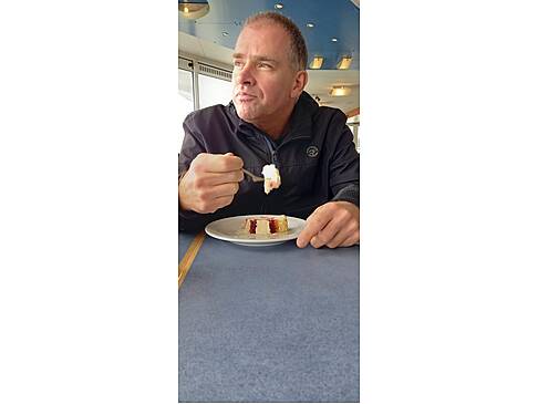 Ein Mann ist Kuchen und schaut aus dem Schiff raus.