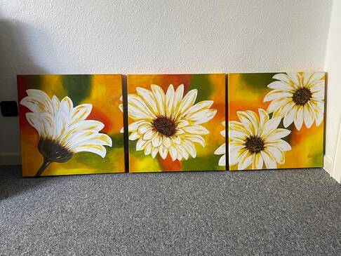 Ein dreiteiliges Gemälde mit einer weißen Blume steht auf einem Boden.