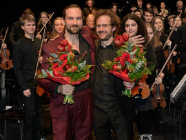 Zwei Herren mit Blumensträßen vor dem Orchester.