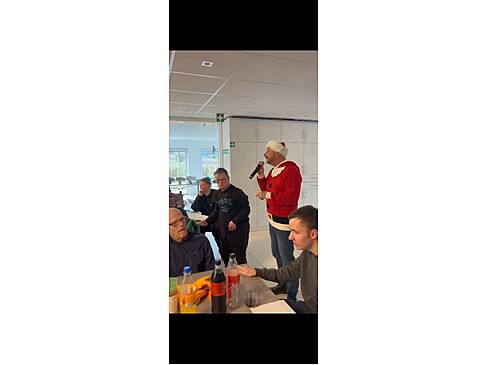 Ein Mann im roten Pulli und einer Nikolausmütze spricht in ein Mirkofon.