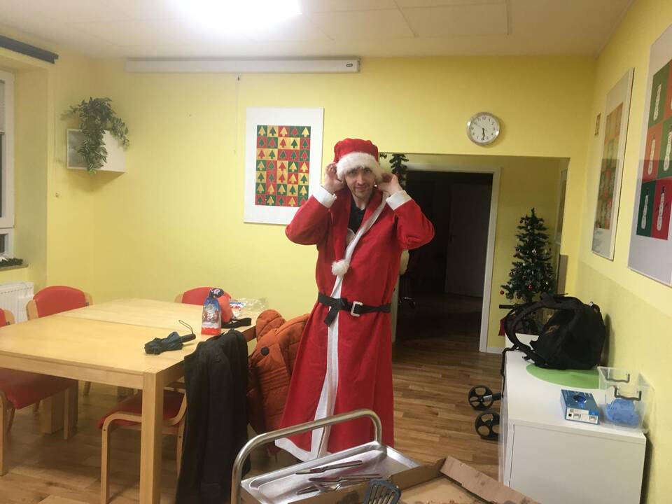 Eine Person im Nikolausmantel zieht sich eine Nikolausmütze an.