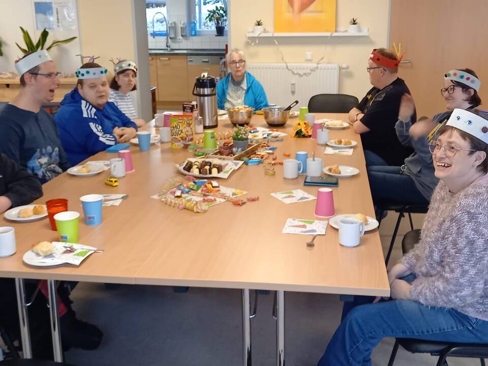 Mehrere Personen sitzen an einem gedeckt und geschmückten Tisch.