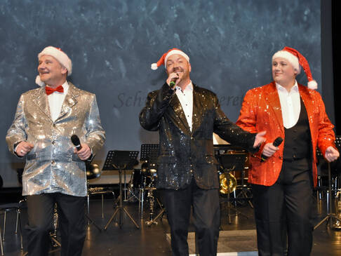 Drei Männer in Glitzersakkos und Weihnachtsmannmütze.