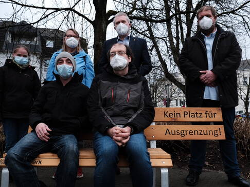 Menschen auf und hinter der Bank mit dem Bürgermeister.