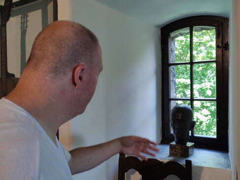 Ein Mann steht vor einem kleinen Fenster und greift nach einer Figur.