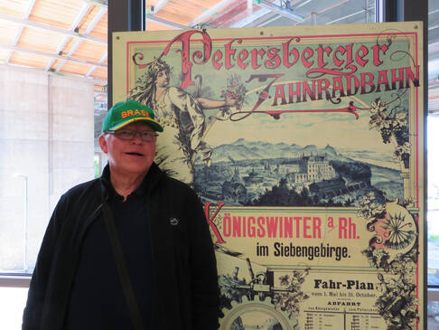 Ein Mann vor einem alten Plakat der Zahnradbahn.