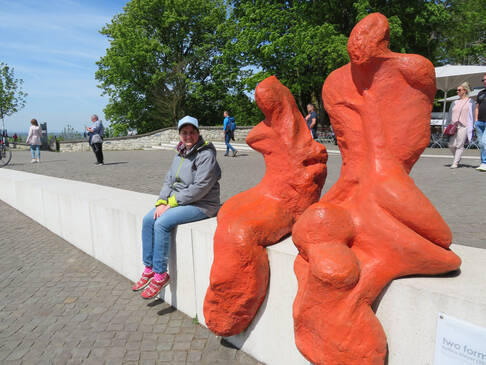 Eine Person sitzt auf einer Mauer neben zwei Skulpturen.