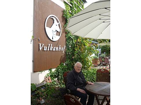 Man sitztam Tisch vor einem Schild vom Vulkanhof.