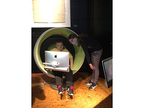 Junge sitzt vor Apple Computer Junge Frau schaut auf Monitor.