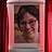 Ein Bild einer Frau mit Brille, links und rechts ein roter Vorhang.