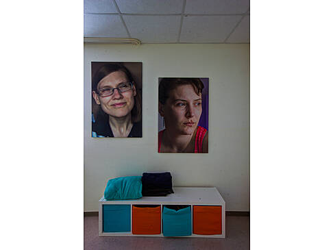 Zwei Bilder mit Frauen hängen an der Wand darunter steht ein Regal auf dem Boden.