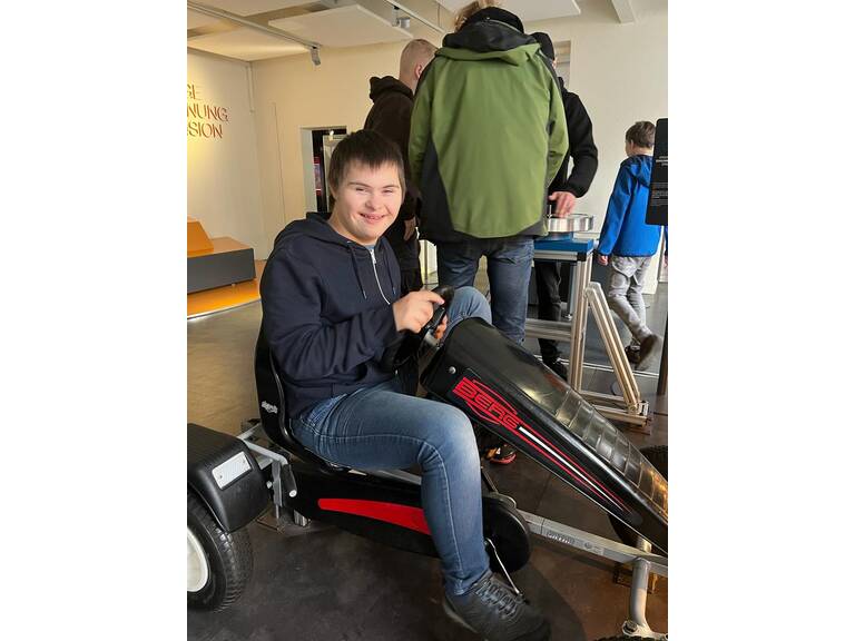 Ein Jugendlicher sitzt auf einem großen Kettcar.