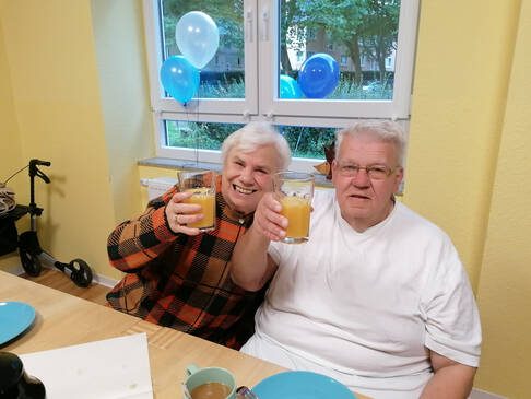 Zwei Personen heben Gläser mit gelber Flüssigkeit.